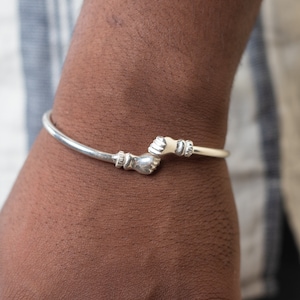 May include: A silver bracelet with two clasped hands as the clasp. The bracelet is on a person's wrist.