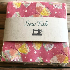 May include: A stack of pink fabric squares with a white polka dot pattern and a butterfly print. The fabric is wrapped in brown paper with the text "Sew Fab" and a sewing machine icon.