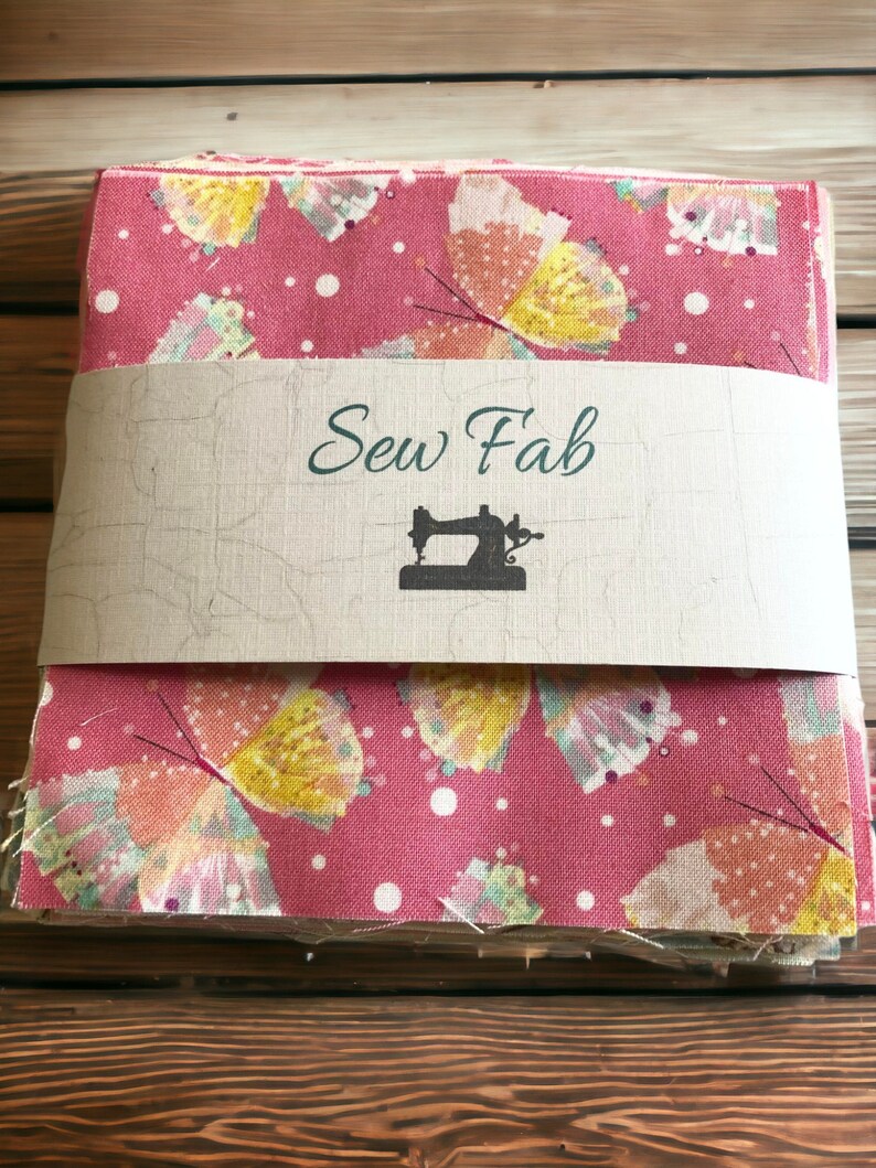 May include: A stack of pink fabric squares with a white polka dot pattern and a butterfly print. The fabric is wrapped in brown paper with the text "Sew Fab" and a sewing machine icon.