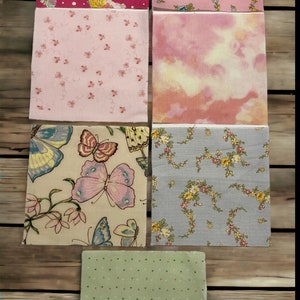 May include: Assortment of six fabric squares with different patterns. The patterns include butterflies, flowers, and polka dots. The fabrics are in shades of pink, green, beige, and gray.