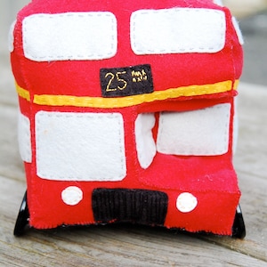 May include: A red felt toy bus with white windows and a black number "25" on the side. The bus has a yellow stripe and white circles on the front.