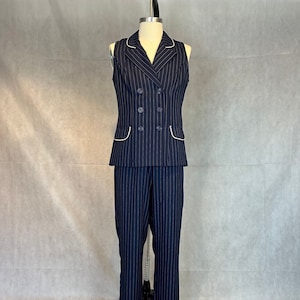 May include: A navy blue pinstripe pantsuit with a double-breasted sleeveless vest. The vest has white piping around the edges and four buttons down the front. The pants have a straight leg.