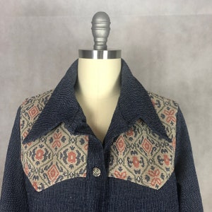 May include: A navy blue button-up shirt with a large collar and a geometric patterned fabric detail on the shoulders and chest.