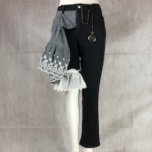 May include: Black denim pants with a gray and white ruffle detail on the left leg. The pants have a pocket on the right side with a pocket watch attached.