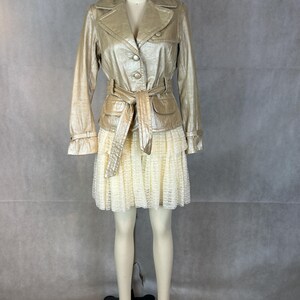May include: A gold metallic jacket with a belt and a white lace skirt. The jacket has a button closure and a collar.