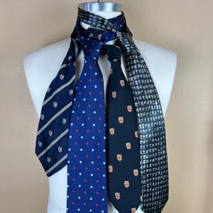 Puede incluir: Cuatro corbatas estampadas se exhiben en un maniquí. Las corbatas incluyen azul marino con rayas blancas, una corbata azul con estrellas rojas y blancas, una corbata azul marino con escudos y una corbata negra con un patrón repetido.