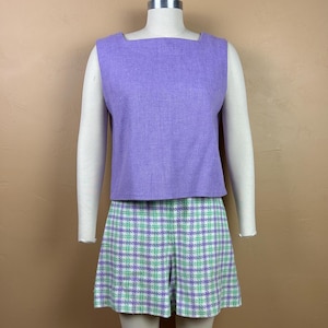 May include: A vintage two-piece outfit comprising a lavender sleeveless top and matching shorts. The top has a square neckline. The shorts feature a plaid pattern in white, green, and lavender. The outfit is displayed on a mannequin.
