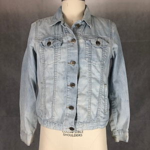 May include: A light blue denim jacket with a button closure and two front pockets. The jacket has a classic style and is in good condition.