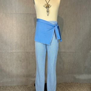 May include: Blue and white patterned pants with a blue wrap-around sash. The sash is tied at the waist and has a long, flowing end. The pants are on a mannequin.