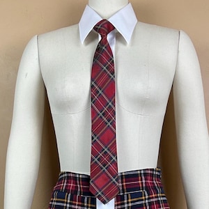 May include: A red necktie featuring a dark blue, yellow, and white plaid pattern, worn with a crisp white collared shirt and a matching red, blue, and yellow plaid skirt. The necktie is tied in a standard knot and hangs centered over the shirt.
