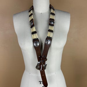 May include: A brown leather belt with silver-toned metal accents and decorative beads. The belt features a buckle and is displayed on a mannequin. The text "T 6 COLLAPSIBLE SHOULDERS" is visible.