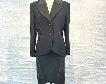 Puede incluir: Un traje negro de dos piezas exhibido en un maniquí. El traje incluye una blazer con solapa de muesca y dos botones, y una falda hasta la rodilla. La blazer tiene detalles de cuero. El traje está hecho de una tela oscura.