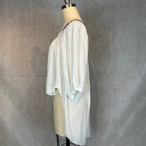 Puede incluir: Blusa blanca, ligera y semitransparente, con un dobladillo alto-bajo y detalles bordados alrededor del escote. La blusa tiene un ajuste holgado y mangas 3/4.
