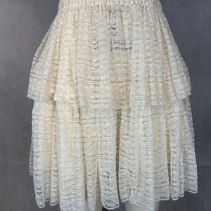 May include: A white lace skirt with multiple layers and a ruffled hem. The skirt has an elastic waistband.