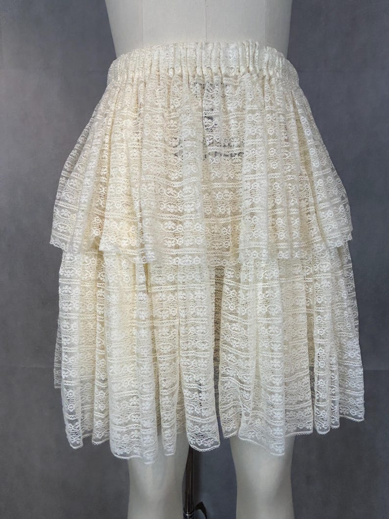 May include: A white lace skirt with multiple layers and a ruffled hem. The skirt has an elastic waistband.
