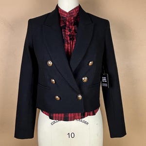 May include: A black cropped blazer with gold buttons and a double-breasted closure. The blazer has a notched collar and long sleeves. The blazer is on a white mannequin.