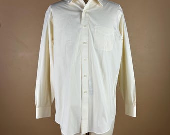 May include: A long-sleeved, cream-colored button-down shirt with a chest pocket. The shirt is displayed on a mannequin, showcasing its classic design and tailored fit. The fabric appears to be a lightweight material.