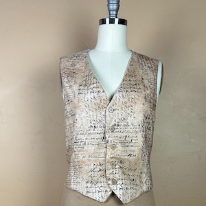 Pode incluir: Um colete bege com decote em V e três botões. O colete é coberto por um padrão de escrita vintage em tinta preta. O colete é exibido em um manequim.