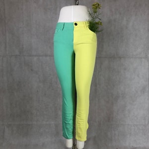 May include: A pair of slim-fit jeans, split vertically with a mint green and yellow color scheme. The jeans have a button and zipper closure, with standard pockets. The garment is displayed on a mannequin.