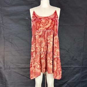 Könnte beinhalten: Ein rotes und cremefarbenes, ärmelloses Minikleid mit floralem Muster und einem Stufenrock. Das Kleid ist aus einem weichen, samtigen Stoff.