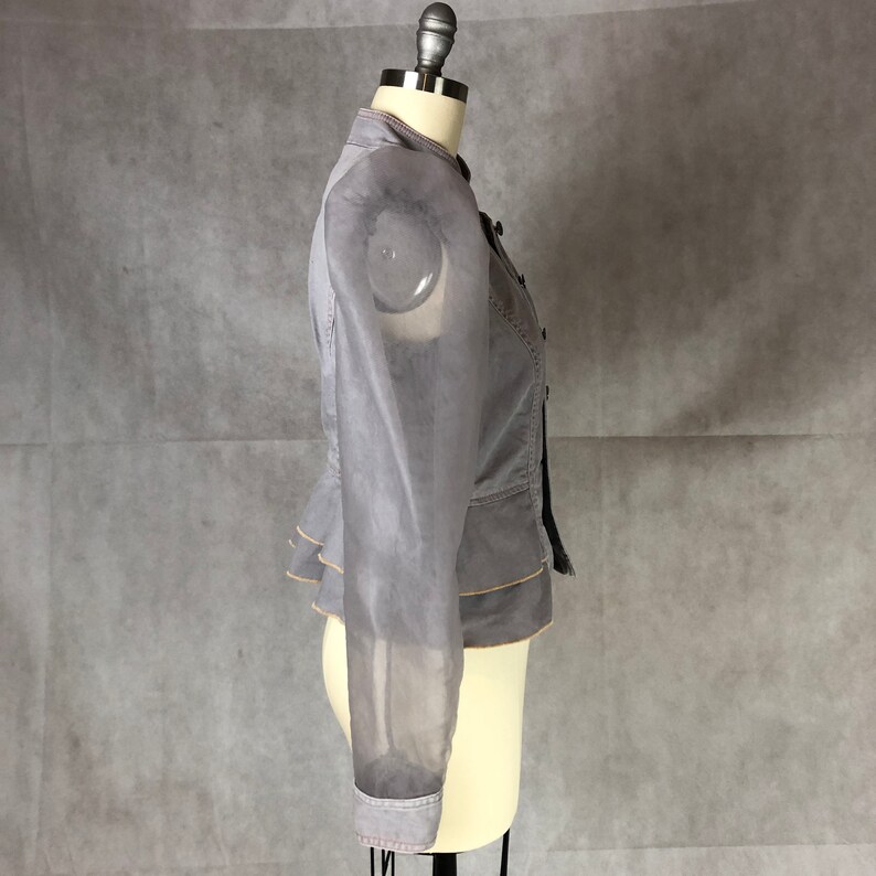K&ouml;nnte beinhalten: Eine graue Jacke mit einem durchsichtigen &Uuml;berzug und einem R&uuml;schen-Saum. Die Jacke hat einen Stehkragen und lange &Auml;rmel.