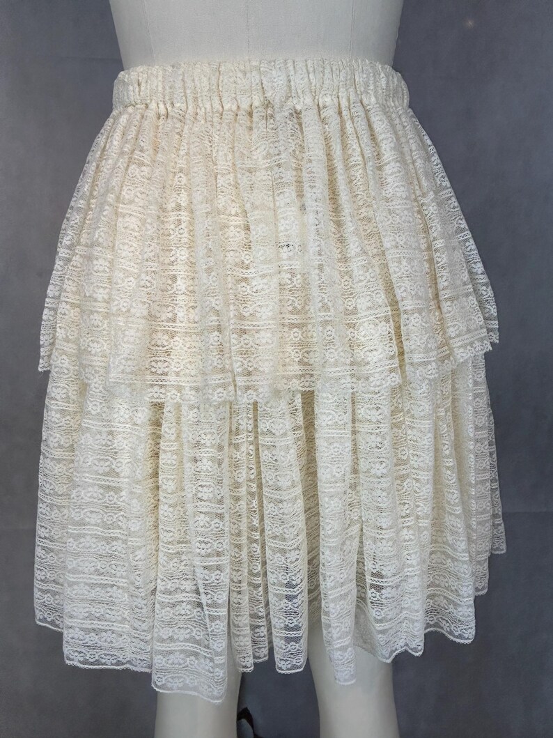 May include: A white lace skirt with a tiered design. The skirt has an elastic waistband and is made of a delicate, sheer fabric.