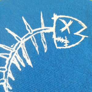K&ouml;nnte beinhalten: Ein wei&szlig;es Fischskelett-Design auf einem blauen Stoffhintergrund.