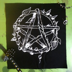 May include: A white pentagram with a wooden frame and a beaded border. The pentagram is surrounded by thorns and leaves. The design is on a black fabric background.