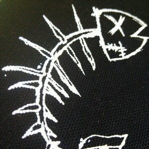 K&ouml;nnte beinhalten: Wei&szlig; gesticktes Design eines Fischskeletts auf schwarzem Stoffhintergrund.