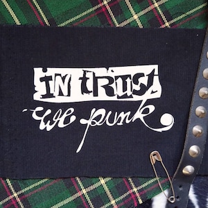 Może przedstawiać: Czarno-biała łatka punk rockowa z tekstem "In trust we punk" na zielono-czerwonym tle w kratę.