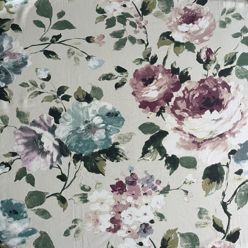 May include: A beige fabric with a floral pattern featuring large pink, white, and teal roses. The fabric has a subtle texture and a vintage aesthetic.