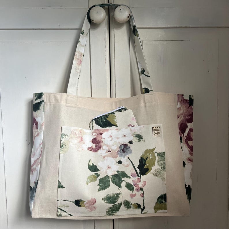 May include: A large beige tote bag with a floral print pocket. The bag has a floral print on the sides and a small label that says "Made with Love".