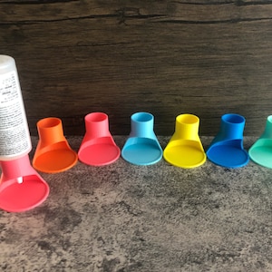 May include: Seven colorful plastic bottle stoppers in various shades of blue, yellow, orange, and pink. The stoppers are designed to fit on top of bottles to keep the contents fresh.