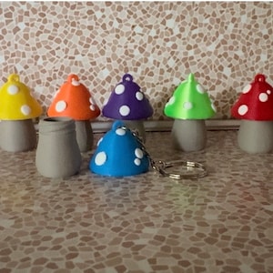 May include: A collection of colorful mushroom-shaped figurines with white polka dots on their caps. The mushrooms are in various colors, including pink, yellow, orange, purple, green, and red. One blue mushroom is attached to a keychain. The stems are gray.