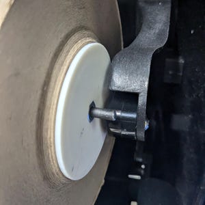 May include: Close-up of a large roll of brown paper towels inside a black dispenser. The roll is mounted on a white plastic disc and a metal rod. The dispenser's black arm holds the roll in place.