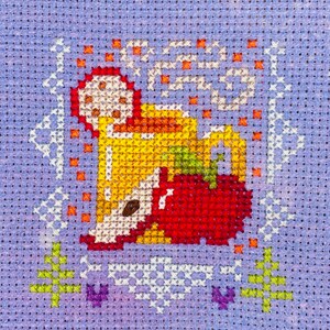 May include: Cross-stitch pattern of a mug of hot beverage with steam rising from it, a red apple, and orange and yellow accents on a purple background.