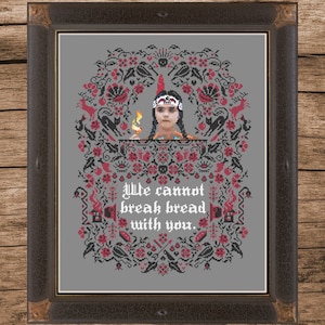Puede incluir: Un patrón de punto de cruz con una niña con un tocado de nativo americano sosteniendo una antorcha. El patrón está rodeado por un borde floral y el texto "We cannot break bread with you."