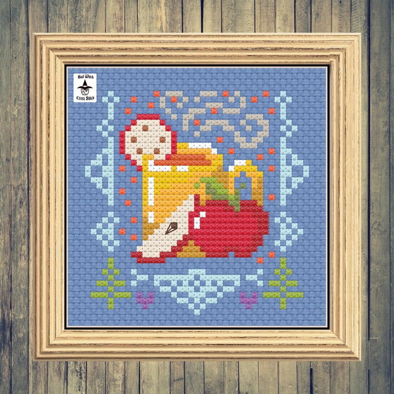 May include: Cross stitch pattern of a mug of apple cider with a red apple and a cinnamon stick. The pattern is on a blue background with a white border. The text "Bad Witch Cross Stitch" is in the top left corner.