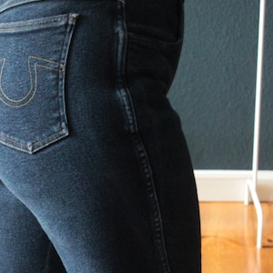 Könnte beinhalten: Dunkelblaue Jeans aus Denim mit einem hufeisenförmigen Logo auf der Gesäßtasche und Knie-Patches.