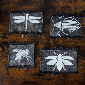 Könnte beinhalten: Sechs Stoffpatches mit verschiedenen Insektenmotiven. Die Patches sind aus dunkelgrauem Stoff mit weißen Insektenmotiven und aus blauem Stoff mit violetten Insektenmotiven.