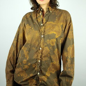 Könnte beinhalten: Ein langärmliges Hemd mit Knöpfen und einem Batik-Muster in Braun- und Beigetönen.