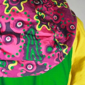 May include: A green and yellow hooded jacket with a pink and green patterned hood. The hood has a floral design with green, pink, and yellow accents.