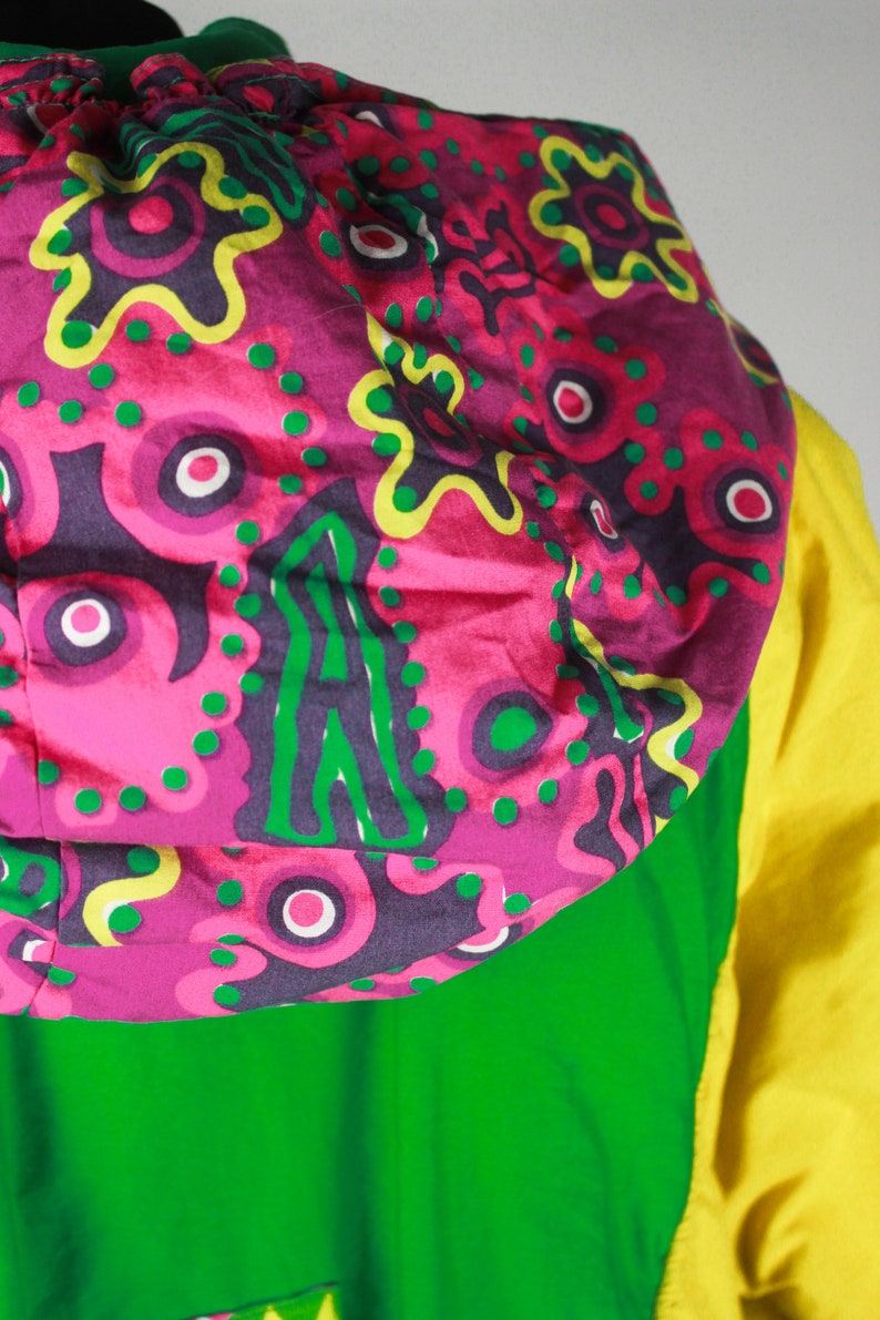 May include: A green and yellow hooded jacket with a pink and green patterned hood. The hood has a floral design with green, pink, and yellow accents.