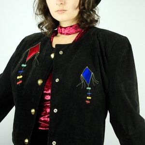 May include: A black suede jacket with a red and blue diamond-shaped design on the front. The jacket has gold buttons and a red velvet lining.