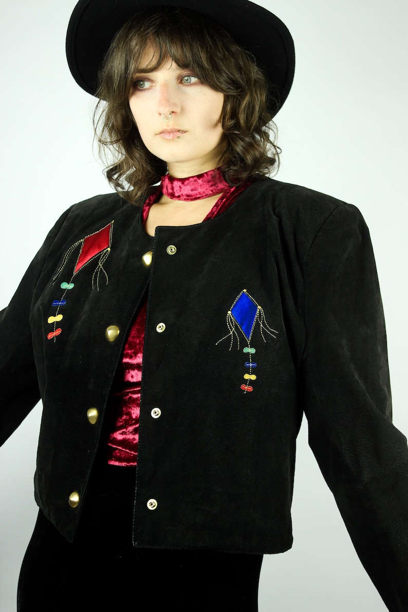May include: A black suede jacket with a red and blue diamond-shaped design on the front. The jacket has gold buttons and a red velvet lining.