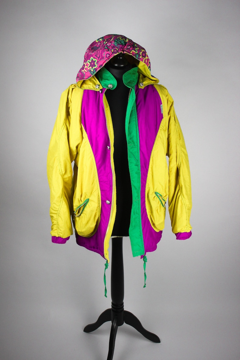 May include: A yellow, pink and green hooded jacket with a floral pattern on the hood. The jacket has a zip fastening and two pockets on the front.