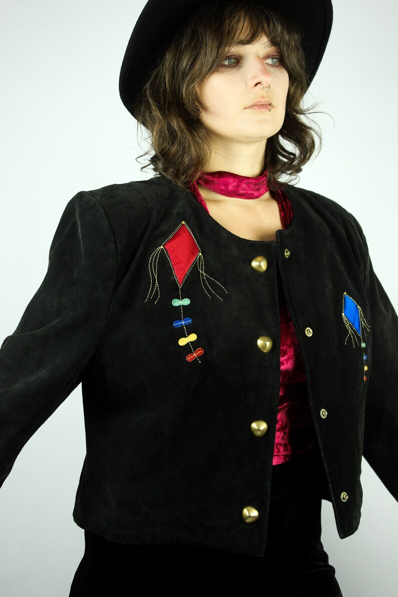 May include: A black suede jacket with a red and blue diamond-shaped design embroidered on the front. The jacket has gold buttons and a red velvet collar.
