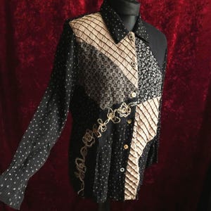 Könnte beinhalten: Schwarzes Langarmhemd mit Patchwork-Design. Das Hemd hat eine Mischung aus Mustern, darunter Punkte, Blumen und geometrische Formen, mit beige und goldenen Akzenten. Goldene Blumenstickerei und Knöpfe zieren die Vorderseite.