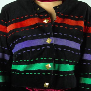 May include: A black suede jacket with colorful striped panels. The jacket has a button closure and gold-toned pyramid-shaped buttons.