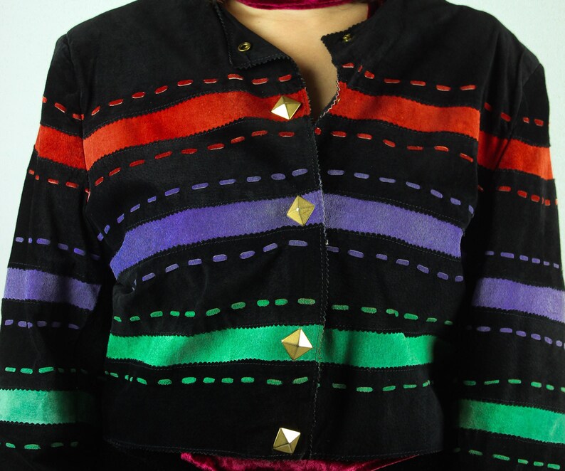 May include: A black suede jacket with colorful striped panels. The jacket has a button closure and gold-toned pyramid-shaped buttons.